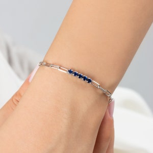 May include: A silver chain bracelet with a row of small blue gemstones.