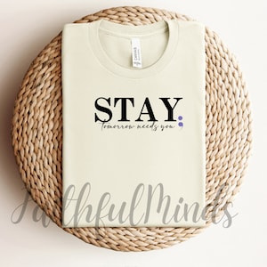 May include: A light green t-shirt with the text "STAY, tomorrow needs you" in black with a purple semicolon.