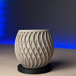 May include: A white ceramic planter with a woven pattern. The planter is sitting on a black circular base.