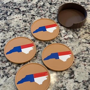 May include: Set of four round tan coasters with a North Carolina state outline design in blue, red, and white. A matching brown coaster holder is also included. These coasters are designed to protect surfaces from drink condensation.