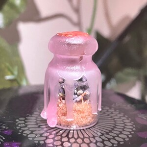 May include: A small glass jar with a pink, dripping glaze. The jar contains brown sugar and dried herbs.