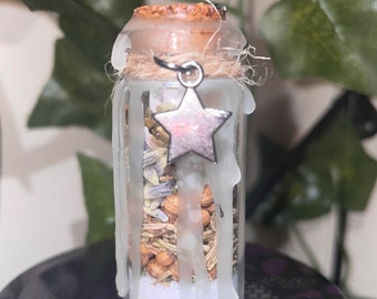 May include: A small glass bottle with a cork stopper and a silver star charm. The bottle is filled with dried herbs and white crystals. The bottle is sealed with white wax.