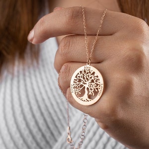 May include: A gold-toned necklace with a tree of life pendant. The pendant is round and features a detailed tree design with the names "Alex", "Atley", and "Lorelei" engraved around the edge.