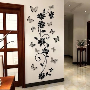 Könnte beinhalten: Wandaufkleber mit einem schwarzen floralen Rankenmuster und mehreren schwarz-weißen Schmetterlingen. Der Aufkleber ist auf einer weißen Wand angebracht und bildet einen dekorativen Akzent. Die Schmetterlinge sind in verschiedenen Größen.