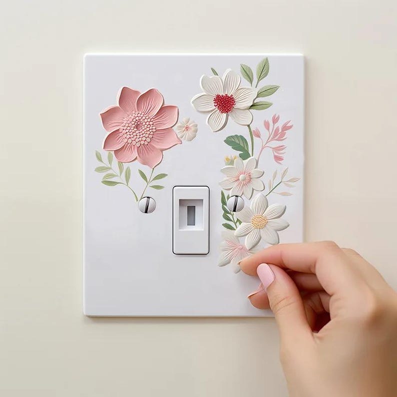 May include: White light switch cover decorated with 3D floral designs in pink, white, and green. The flowers are arranged around the switch and include a large pink flower and several smaller white flowers.