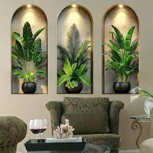 Op de afbeelding: Drie muurstickers met gewelfde nissen in gouden lijsten, elk met een groene plant in een pot. De linker- en rechterstickers tonen bananenplanten in zwarte potten, terwijl de middelste sticker een palmplant in een zwarte pot toont.