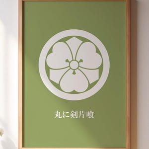 Könnte beinhalten: Ein gerahmter Druck mit einem weißen Blumenemblem auf grünem Hintergrund. Der Druck befindet sich in einem Holzrahmen und hängt an einer weißen Wand. Japanischer Text befindet sich unter dem Emblem. Der Druck wird über einem Holztisch angezeigt.