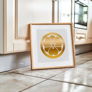 Könnte beinhalten: Ein gerahmter Druck mit einem goldenen Blumenemblem auf weißem Hintergrund. Das Emblem ist eine stilisierte Blume in einem Kreis. Der Rahmen ist aus hellem Holz und der Druck lehnt an einem Schrank.