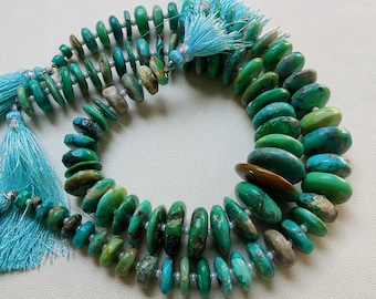 May include: Strands of turquoise gemstone beads in varying shades of green and blue. The beads are disc-shaped and strung together with small white beads. Light blue tassels are attached to the ends of the strands.