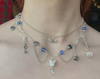 May include: A silver layered necklace with blue beads, charms, and a white porcelain pig pendant.