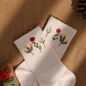 Peut inclure: Une paire de chaussettes blanches avec des fleurs rouges et jaunes brodées. Les chaussettes sont côtelées et ont un look décontracté.