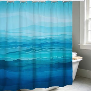 Op de afbeelding: Een blauw douchegordijn met een aquarelontwerp. Het gordijn heeft horizontale banden in verschillende blauwtinten, waardoor een gelaagd, golfachtig patroon ontstaat. Het bovenste gedeelte is lichter en gaat over in diepere blauwtinten aan de onderkant. Het gordijn hangt aan witte ringen.