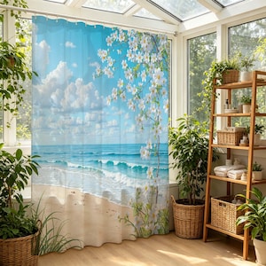 May include: A shower curtain featuring a printed scene of a sandy beach, turquoise ocean waves, and a bright blue sky with white clouds. A branch with white flowers and green leaves extends vertically across the right side of the curtain.