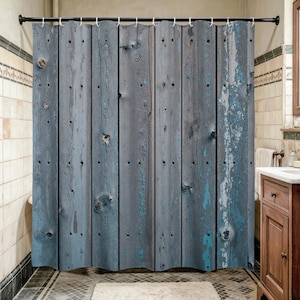 May include: A shower curtain featuring a printed pattern of vertical weathered wooden planks in shades of grey and blue. The design includes realistic wood grain textures, dark knots, and patches of peeling blue paint across the surface.