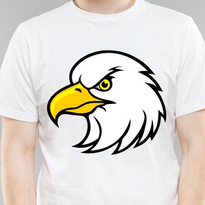 May include: White t-shirt with a black and yellow cartoon eagle head graphic.