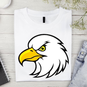 May include: White t-shirt with a black and yellow cartoon eagle head graphic. The eagle has a fierce expression with a yellow beak and a black eye.