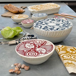 May include: A set of reusable food covers with various colorful patterns. The covers are made of fabric and have a drawstring closure. The covers are shown on bowls and a baking dish.