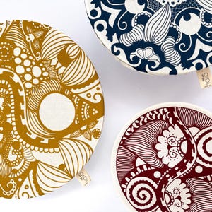 May include: Three round fabric bowl covers with different patterned designs. The covers are white with a gold, blue, and red pattern. The covers have the word "halo" printed on them.