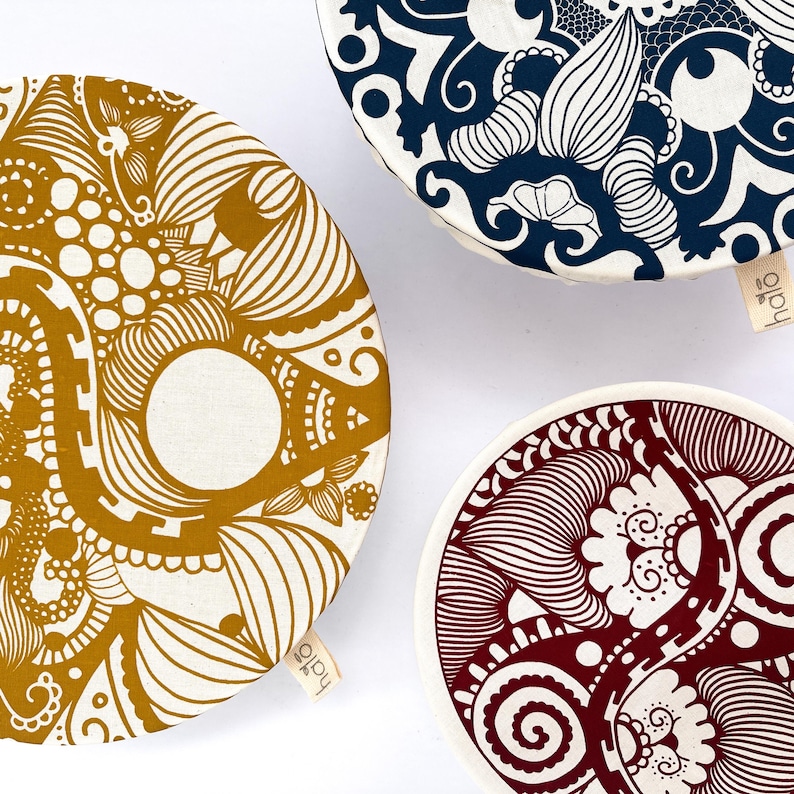 May include: Three round fabric bowl covers with different patterned designs. The covers are white with a gold, blue, and red pattern. The covers have the word "halo" printed on them.