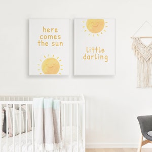 May include: Two white framed prints with yellow sun illustrations and text. The left print says "here comes the sun" and the right print says "little darling".