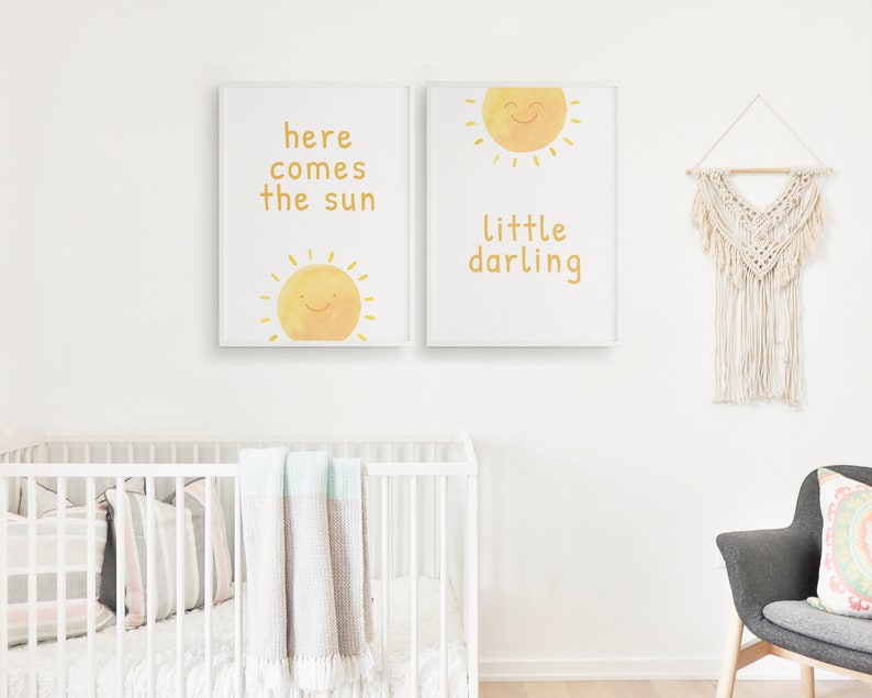 May include: Two white framed prints with yellow sun illustrations and text. The left print says "here comes the sun" and the right print says "little darling".