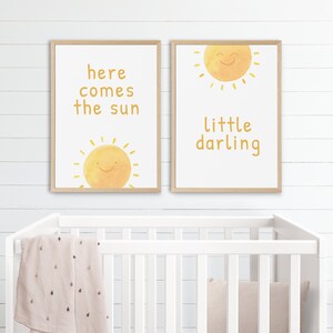 May include: Two framed prints with a yellow sun and text. The left print says "here comes the sun" and the right print says "little darling".