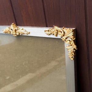 May include: A silver picture frame with ornate gold corner and edge detailing. The frame has a rectangular shape and a neutral background, suitable for displaying photographs or artwork. The gold accents add a touch of elegance.