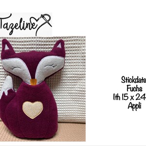 May include: Plush fox toy in shades of burgundy, white, and cream. The fox has closed eyes, a heart-shaped patch on its chest, and a cream-colored heart. The text "Tazeline" is above the fox. The fox measures approximately 15 x 24 cm.