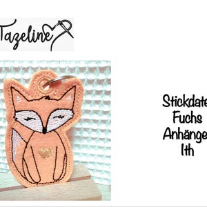 May include: A peach-colored fox keychain with a gold heart and black outline. The fox has white accents and closed eyes. The text "Tazeline" is above the keychain. The text "Stickdatei Fuchs Anhänger Ith" is to the right.