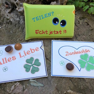 Peut inclure: Trois cartes blanches avec des bordures bleues et des trèfles à quatre feuilles verts. Les cartes portent les inscriptions "Alles Liebe", "Dankeschön" et "Teilen? Echt jetzt!" avec une paire d'yeux de dessin animé. Chaque carte a un bonbon au chocolat sur le dessus.