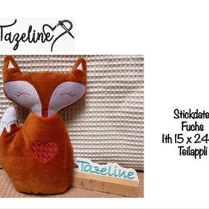 May include: A plush orange fox with white accents and a red heart on its chest. The fox has closed eyes and a small wooden sign with the name "Tazeline". The fox measures approximately 15 x 24 cm.