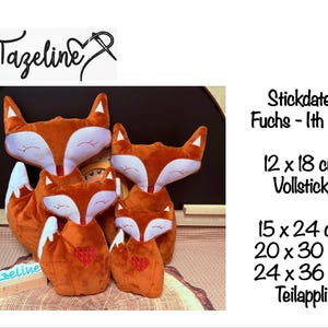 May include: A group of orange fox-shaped cushions with white faces and ears, some featuring a red heart. The image includes the text "Tazeline" and size specifications in centimetres. The cushions vary in size, from 12 x 18 cm to 24 x 36 cm.