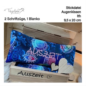 May include: A blue eye pillow with a colourful mandala pattern and the word "AUSZEIT" embroidered in pink. The pillow is in a wooden box with the word "Auszeit" carved into the wood.