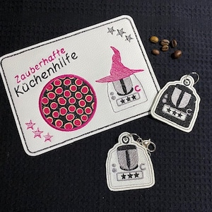 May include: A white card with the text "Zauberhafte Küchenhilfe" and a pink witch hat over a black and white kitchen appliance. There are two black and white kitchen appliance charms with a star rating.