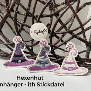 May include: Three embroidered witch hat keychains featuring purple, black, and white stitching with a metal ring attached to each. A circular white button above the hats displays the black text Tazeline with a needle and thread icon.