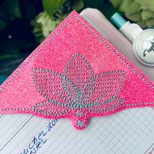 Könnte beinhalten: Rosa glitzernder Lesezeichen mit einem silbernen gestickten Blumendesign. Das Lesezeichen ist dreieckig und hat eine spitze Spitze. Das Lesezeichen befindet sich auf einer Seite eines Planers mit dem Text "eicher 201" und "aster", der mit blauer Tinte geschrieben ist.