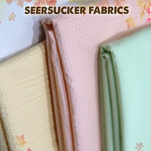 May include: Three different colors of seersucker fabric, including yellow, pink, and green. The fabric is folded and stacked on top of each other.