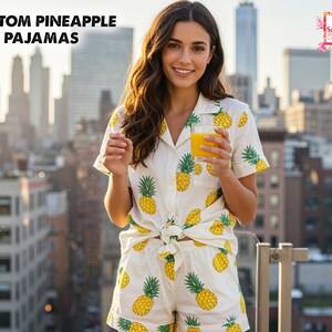 May include: White pajama set with a yellow pineapple pattern. The set includes a short-sleeved, button-down shirt and matching shorts. The text "CUSTOM PINEAPPLE PAJAMAS" is at the top left. The image also includes the text "All Season's Celebrations".
