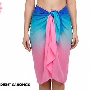 May include: A gradient sarong in shades of blue and pink. The fabric transitions from a deep blue at the top, through turquoise, to a soft pink at the bottom. The sarong is tied at the waist, with the text "GRADIENT SARONGS" at the bottom.