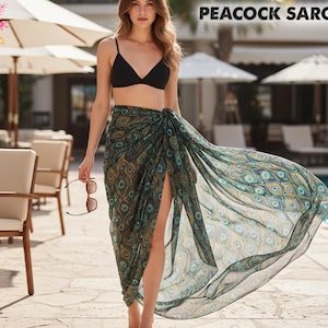 May include: A sheer peacock sarong with a split, featuring a teal, gold, and blue pattern. The sarong is wrapped around the waist. The image also shows a black bikini top and sunglasses.