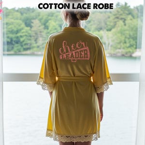 May include: A yellow cotton lace robe with a belt, lace trim, and the words "cheer leader" in glitter on the back. The robe is knee-length and has short sleeves. The text "COTTON LACE ROBE" is at the top.
