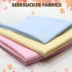 May include: Three different striped seersucker fabrics, one light blue, one yellow, and one pink. The fabrics are folded on top of each other.