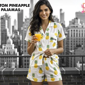 May include: White pajama set with a yellow pineapple pattern. The short-sleeved shirt and shorts are personalized with the name "Ashley". The image also includes the text "CUSTOM PINEAPPLE PAJAMAS".