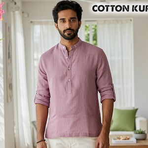 May include: A dusty rose cotton kurta with a mandarin collar and button-down placket. The sleeves are rolled up, revealing the forearms. The text "COTTON KURTA" is displayed at the top of the image.