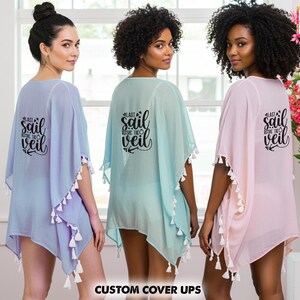 Op de afbeelding: Drie vrouwen dragen doorschijnende cover-ups in pasteltinten: lavendel, mintgroen en roze. Elke cover-up heeft witte kwastjes en de tekst "Last Sail Before The Veil" op de rug. De cover-ups zijn licht en luchtig.