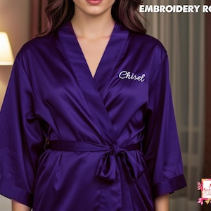 Op de afbeelding: Een dieppaarse satijnen badjas met een wikkelontwerp en een striksluiting. De badjas heeft wijde mouwen en het woord "Chisel" is wit op de voorkant geborduurd. De tekst "EMBROIDERY ROBES" staat bovenaan.