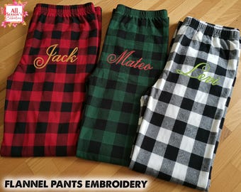 May include: Three pairs of flannel pajama pants in red, green, and black and white buffalo plaid patterns. Each pair has a name embroidered in a cursive font: "Jack", "Mateo", and "Levi". The text "FLANNEL PANTS EMBROIDERY" is at the bottom.