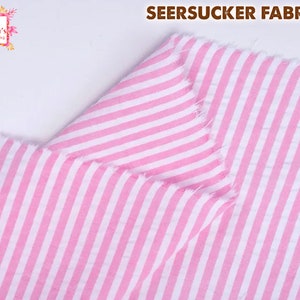 May include: Close-up of pink and white striped seersucker fabric. The fabric is folded, showing the texture and pattern. The words "SEERSUCKER FABRICS" are at the top. The logo for "All Season's Celebrations" is in the upper left corner.