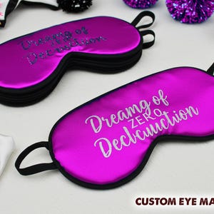 May include: Two purple satin eye masks with black elastic straps. The text on the masks reads "Dreaming of Zero Deconstruction".