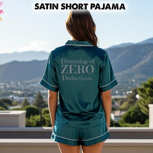 Puede incluir: Conjunto de pijama corto de satén verde azulado con ribete blanco. La parte superior tiene mangas cortas y el texto "Dreaming of ZERO Deductions" en plata. La imagen también incluye el texto "All Season's Celebrations".